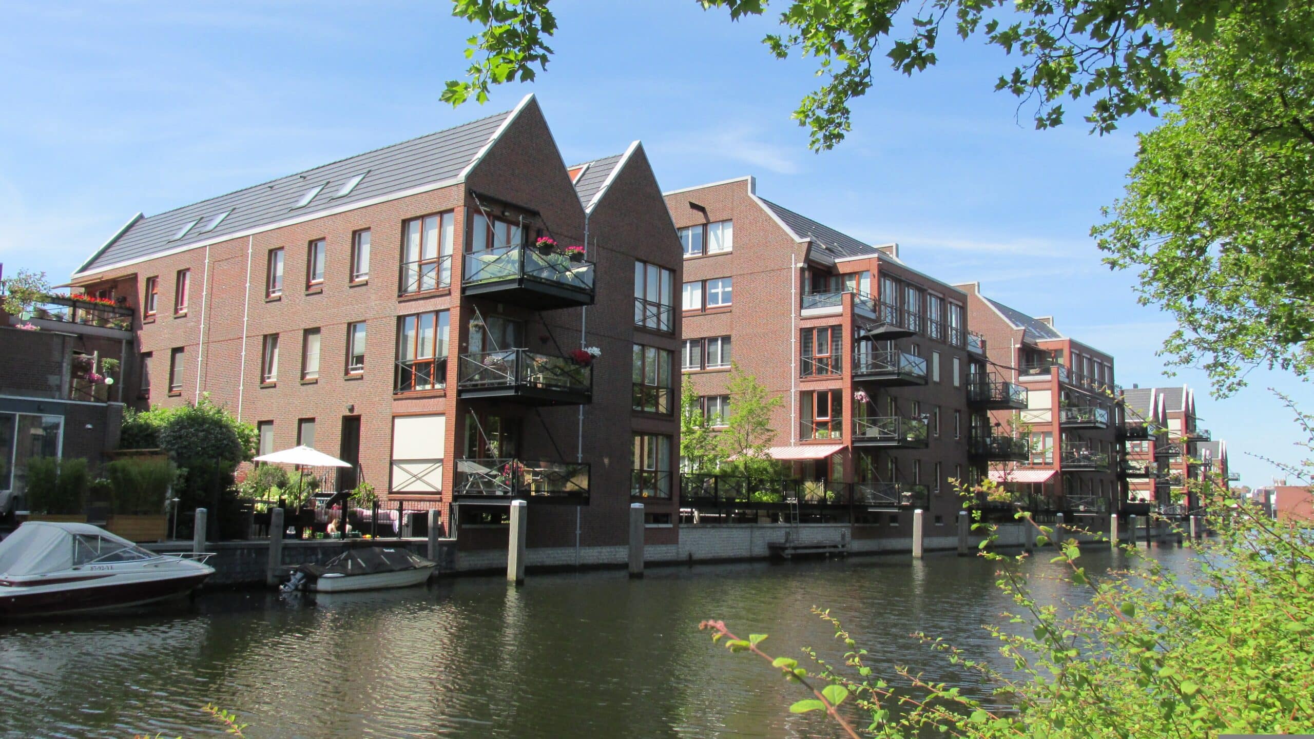 Immeubles résidentiels modernes en briques rouges en bordure de canal, sous un ciel bleu ensoleillé.